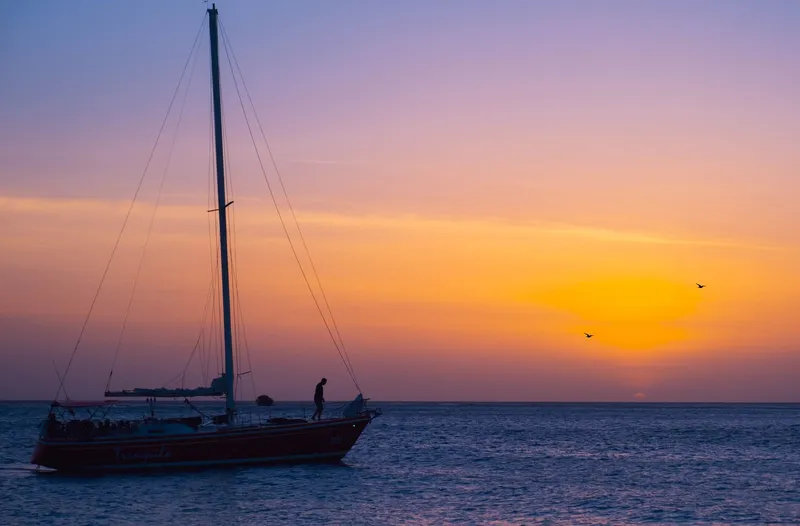Aruba: A tranquil sailboat silhouette against a vibrant sunset over the sea in Aruba.
