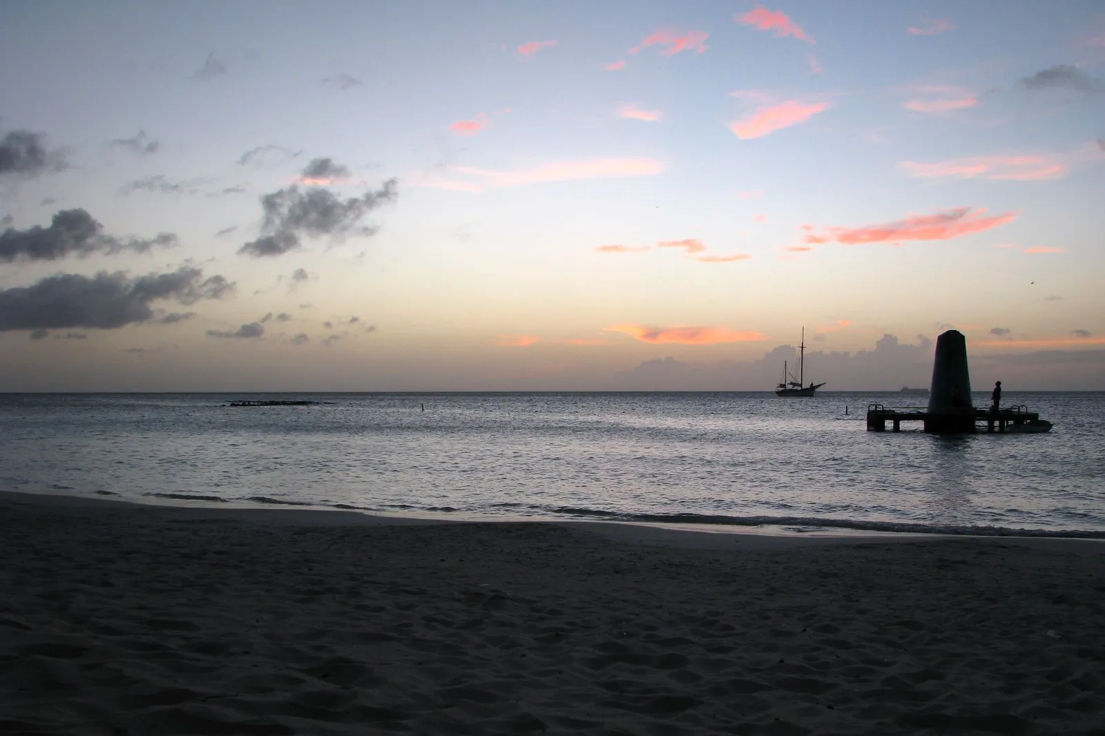 Aruba: Peaceful twilight over Aruba beach with a silhouette of a pier and boat at sea.