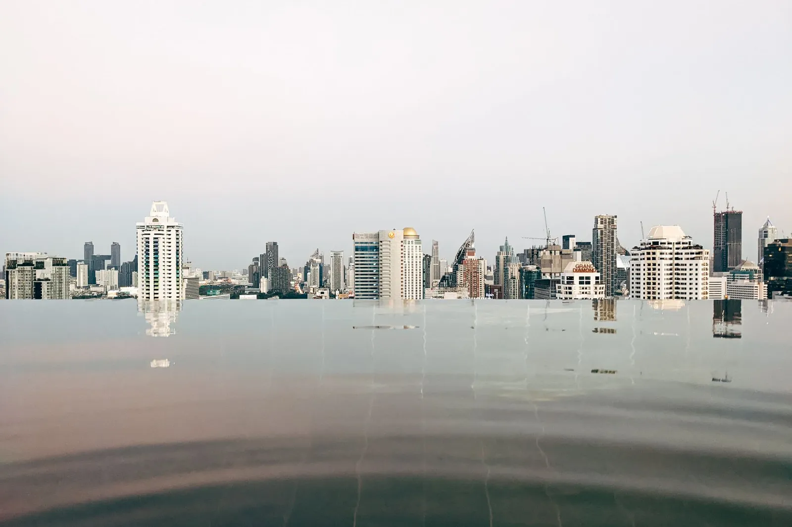 Bangkok: Tranquil infinity pool with reflections of the Bangkok skyline under a calm sky.