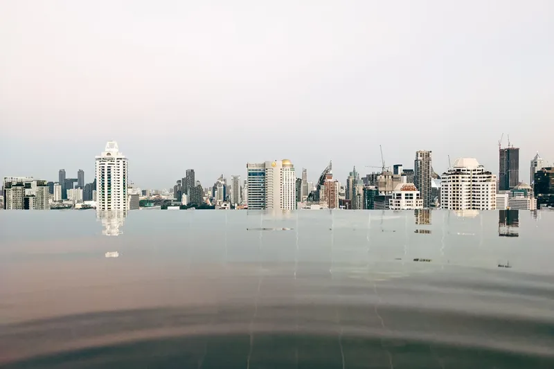 Bangkok: Tranquil infinity pool with reflections of the Bangkok skyline under a calm sky.