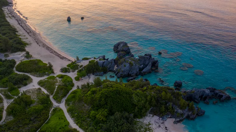 Bermuda: A breathtaking aerial view of Bermuda's coastline during sunset, showcasing clear blue waters and rocky formations.