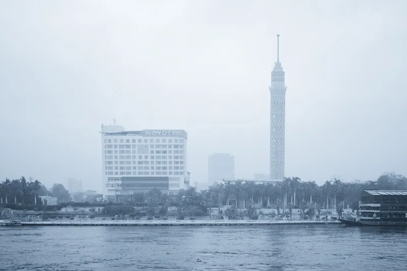 Foggy cityscape of Cairo featuring the Cairo Tower and Novotel by the Nile River.