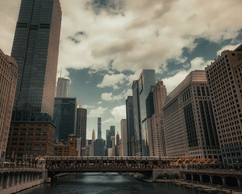 Chicago: A stunning view of Chicago's skyline and river with prominent skyscrapers and bridges on a cloudy day.