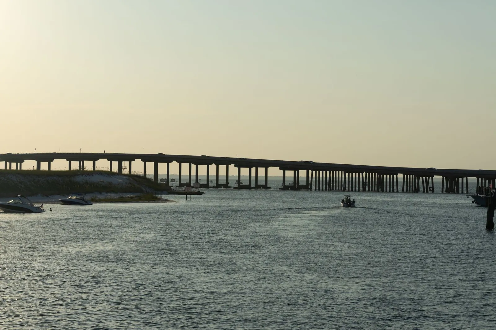 Destin & the Emerald Coast: Peaceful scene of Destin Bridge over calm waters at sunset with boats nearby.