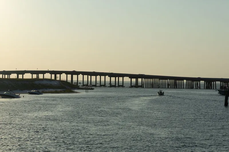 Destin & the Emerald Coast: Peaceful scene of Destin Bridge over calm waters at sunset with boats nearby.