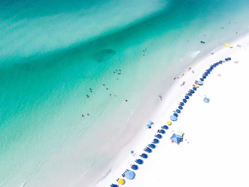 Destin & the Emerald Coast: Stunning aerial view of Santa Rosa Beach showcasing turquoise waters and colorful umbrellas, perfect summer destination.