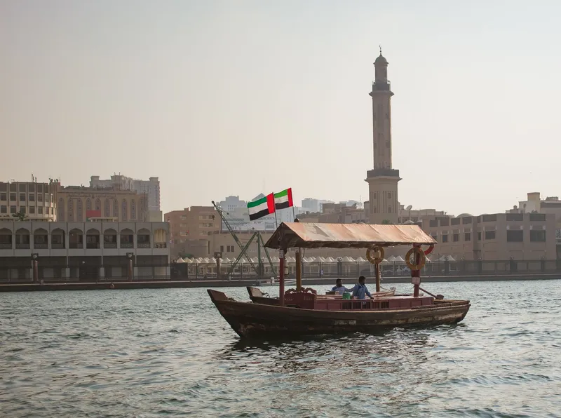 Dubai: A traditional abra boat sails on Dubai Creek with a city skyline and minaret in the background.