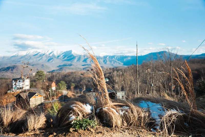 Picturesque landscape of snow-covered mountains, countryside homes, and dry grass in early winter.