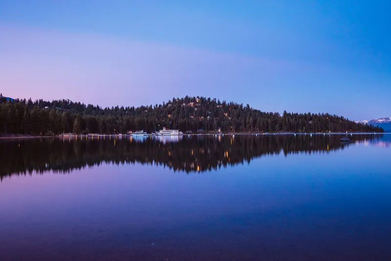 Serene twilight over Lake Tahoe with forested mountain reflections and calm blue waters.