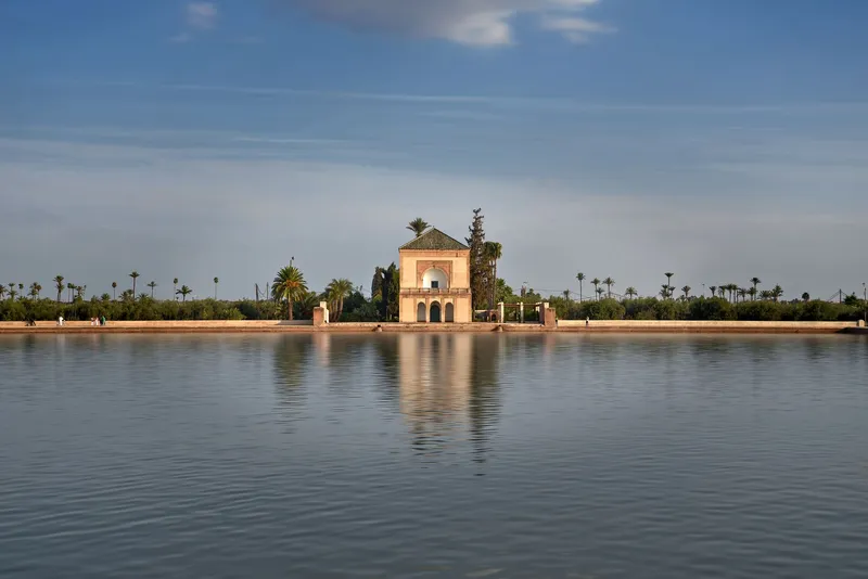 Tranquil view of Menara Gardens pavilion reflecting in water under a clear blue sky in Marrakech.