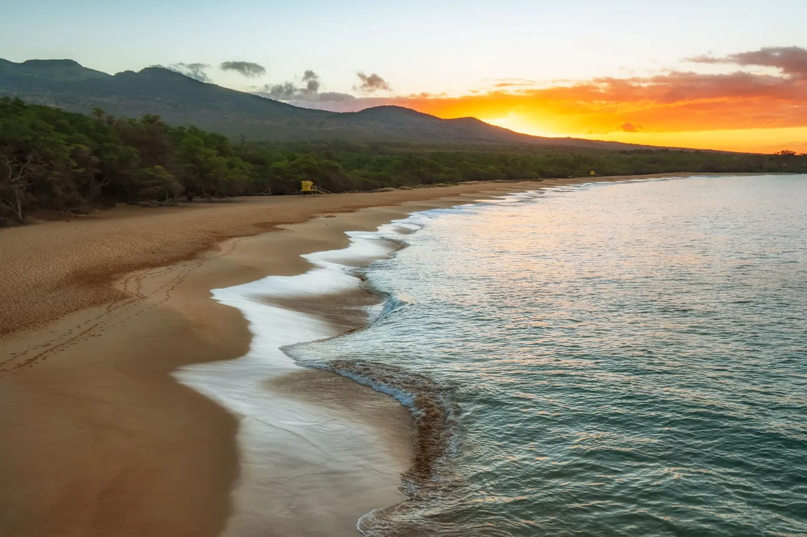 Maui: Serene sunset at Makena Beach, Maui, with ocean waves lapping the shore.
