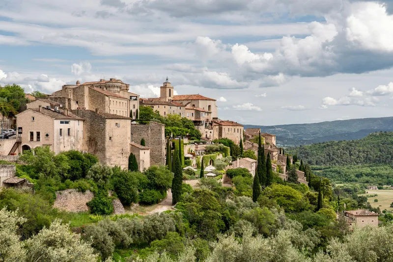 Provence: Picturesque view of a historic hilltop village in Provence surrounded by lush greenery.