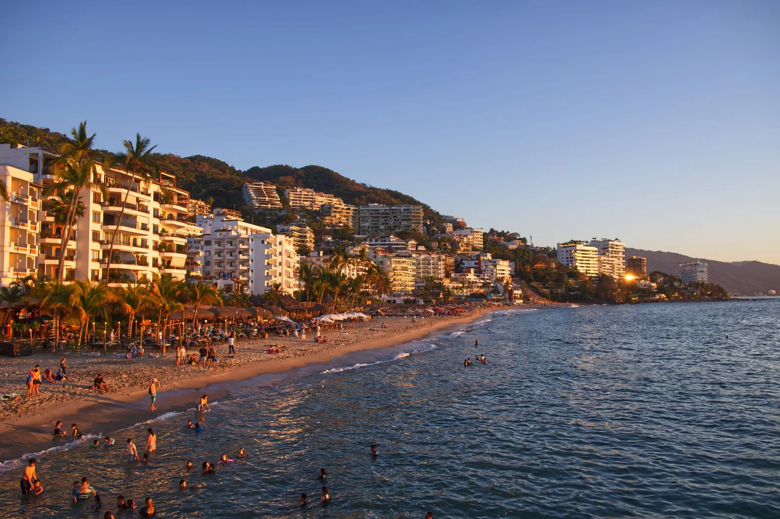Puerto Vallarta: Explore the vibrant coastline of Puerto Vallarta, Mexico with bustling beach activity and scenic resorts at sunset.