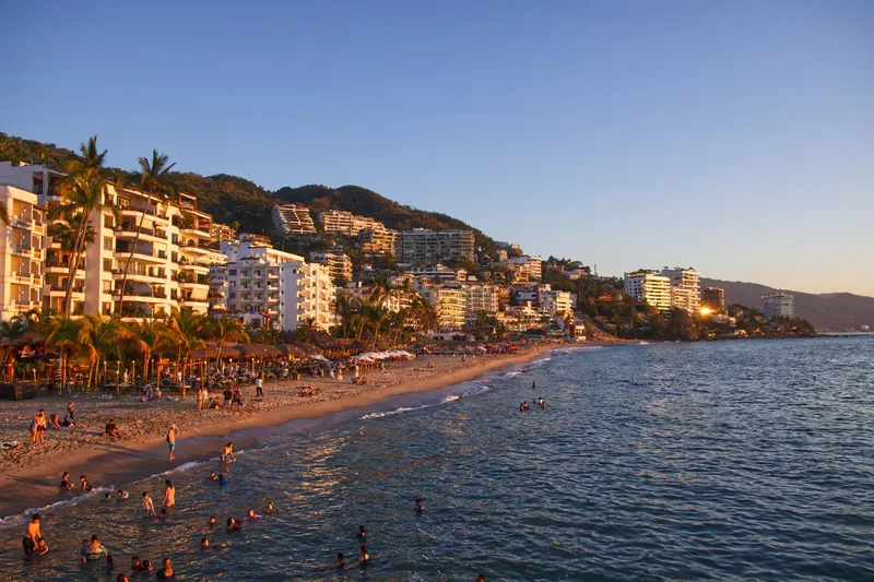 Puerto Vallarta: Explore the vibrant coastline of Puerto Vallarta, Mexico with bustling beach activity and scenic resorts at sunset.