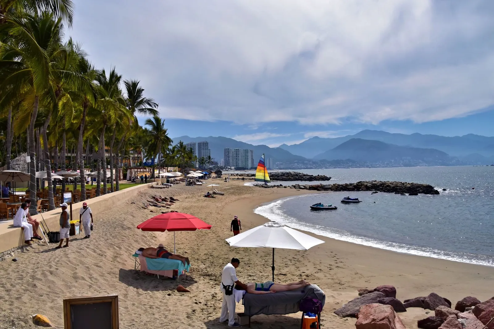 A serene beach view in Puerto Vallarta with palm trees, umbrellas, and a sailboat.