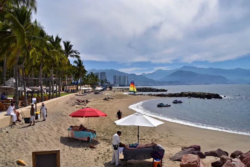 Puerto Vallarta: A serene beach view in Puerto Vallarta with palm trees, umbrellas, and a sailboat.