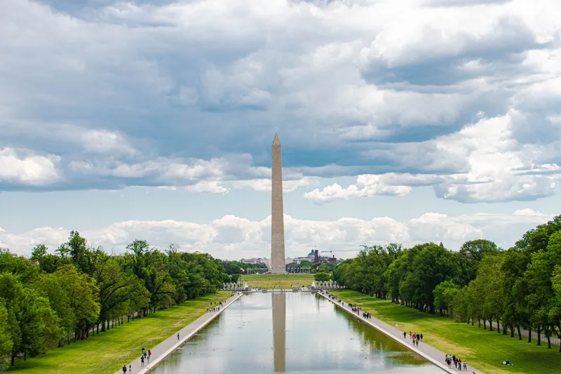 Washington, D.C.: A scenic view of the Washington Monument in Washington, D.C., with reflections in the reflecting pool and a cloudy sky overhead.